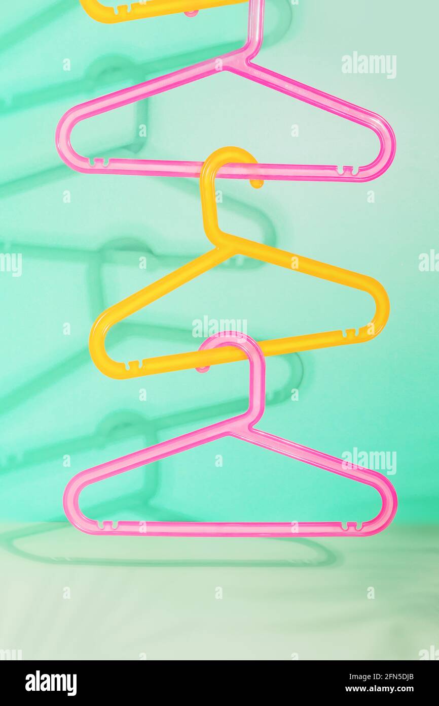 Vertical composition of colored children's plastic hangers hung on top of each other on a light blue background with shadows. The concept of finishing Stock Photo