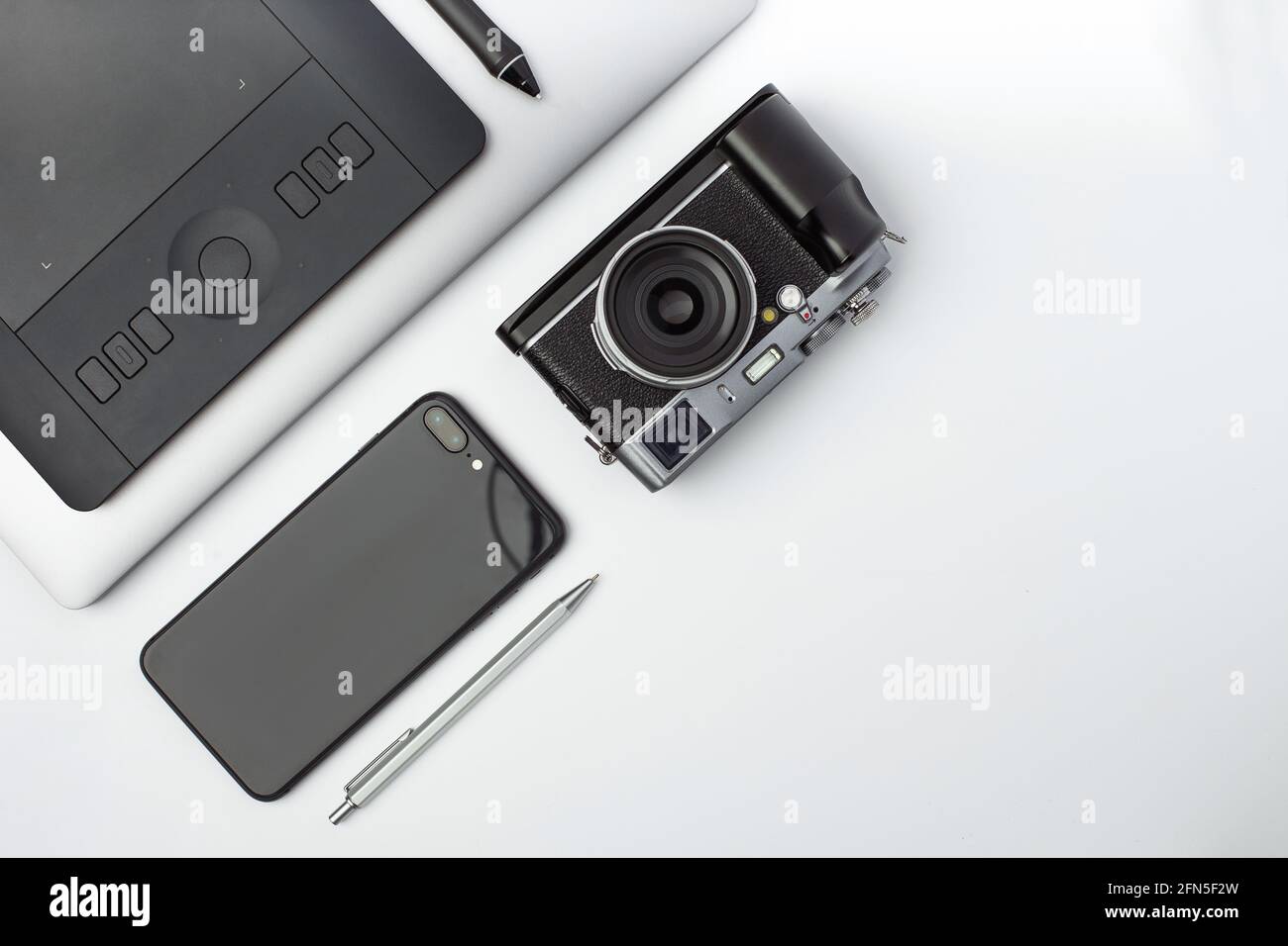 A mirrorless camera, graphic tablet, laptop and black smartphone lays ...
