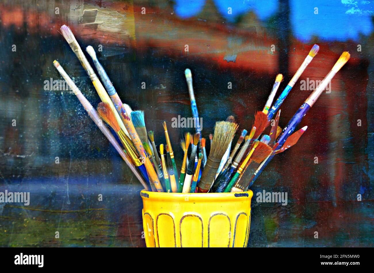 Display of colorful paint brushes in a yellow ceramic jar at the