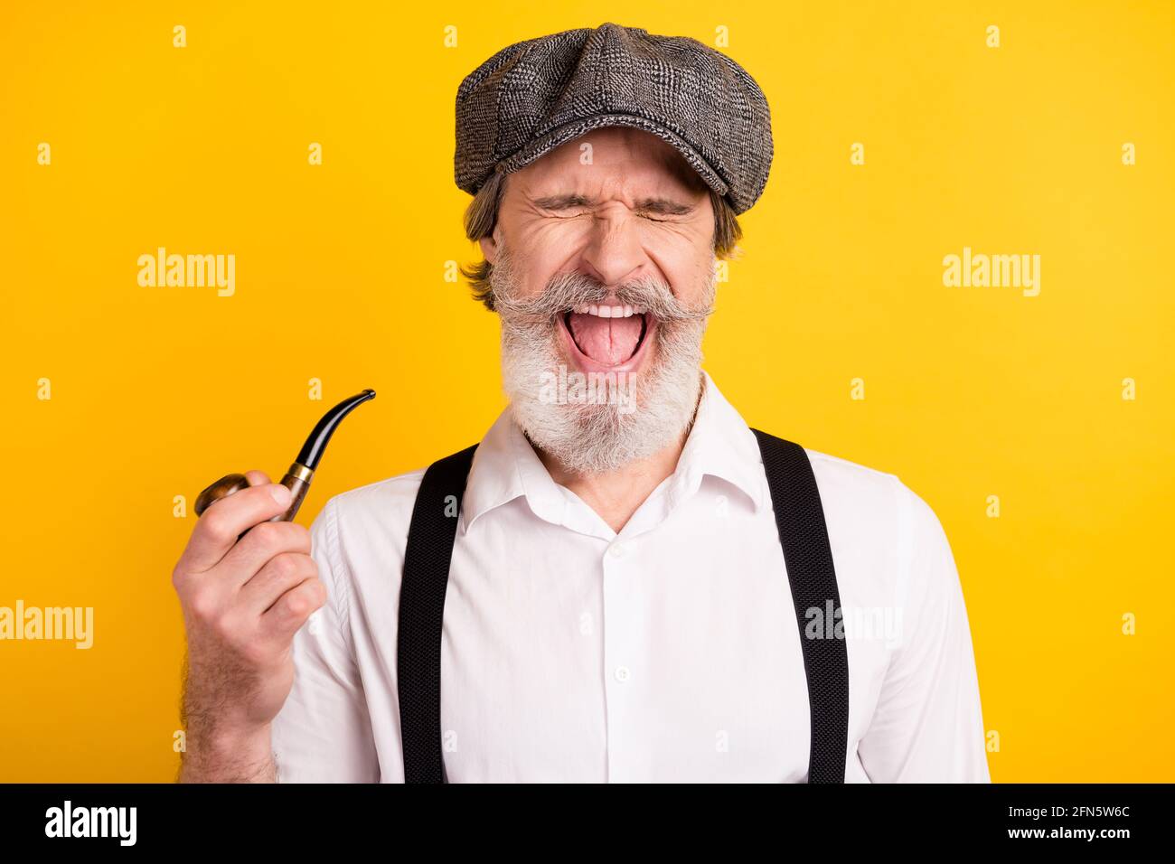 Photo portrait of bearded man laughing in retro outfit smoking wooden pipe smiling isolated vivid yellow color background Stock Photo