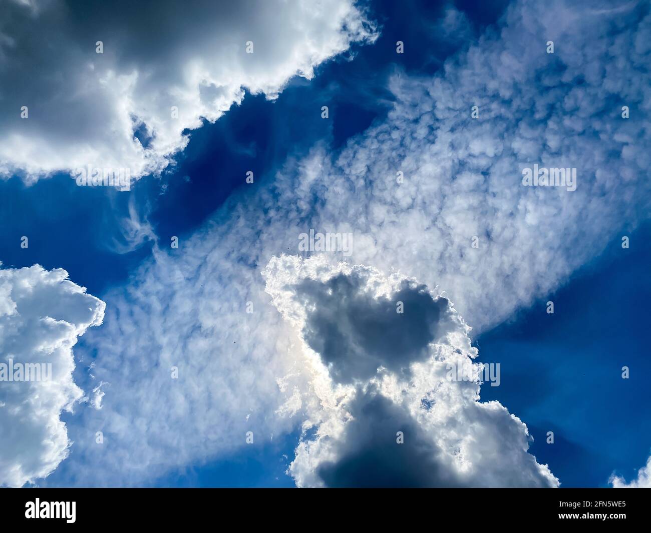 View into blue summer sky with cumulus and cirrocumulus fair weather clouds backlight by sun Stock Photo