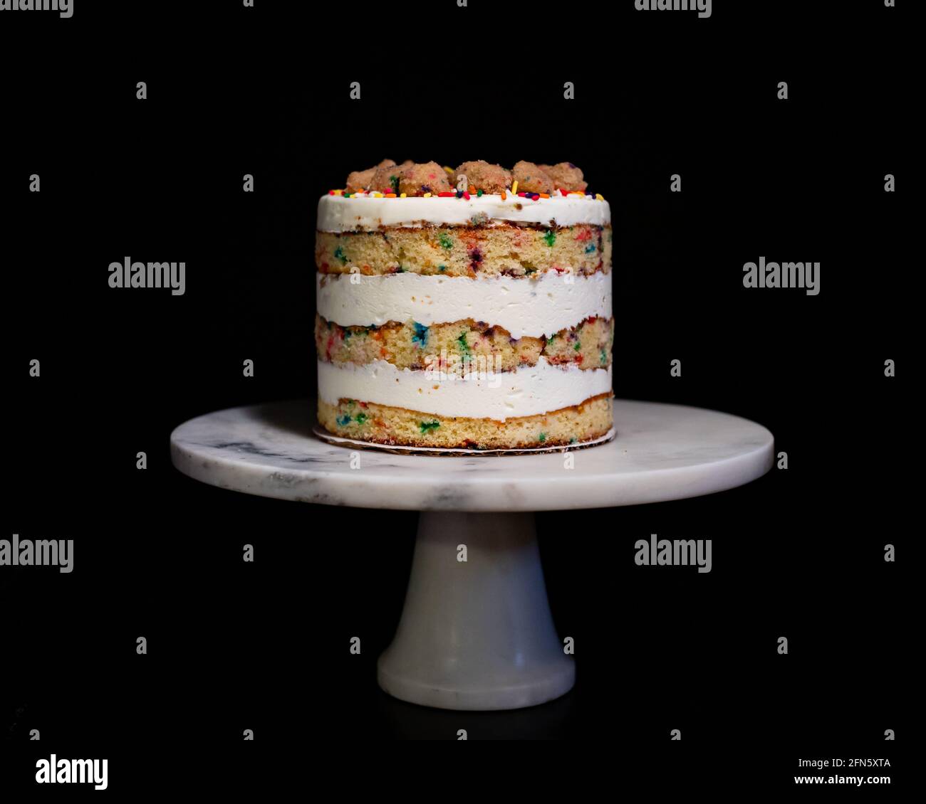 Rainbow Sprinkle Birthday Cake on White Marble Cake Stand Stock Photo