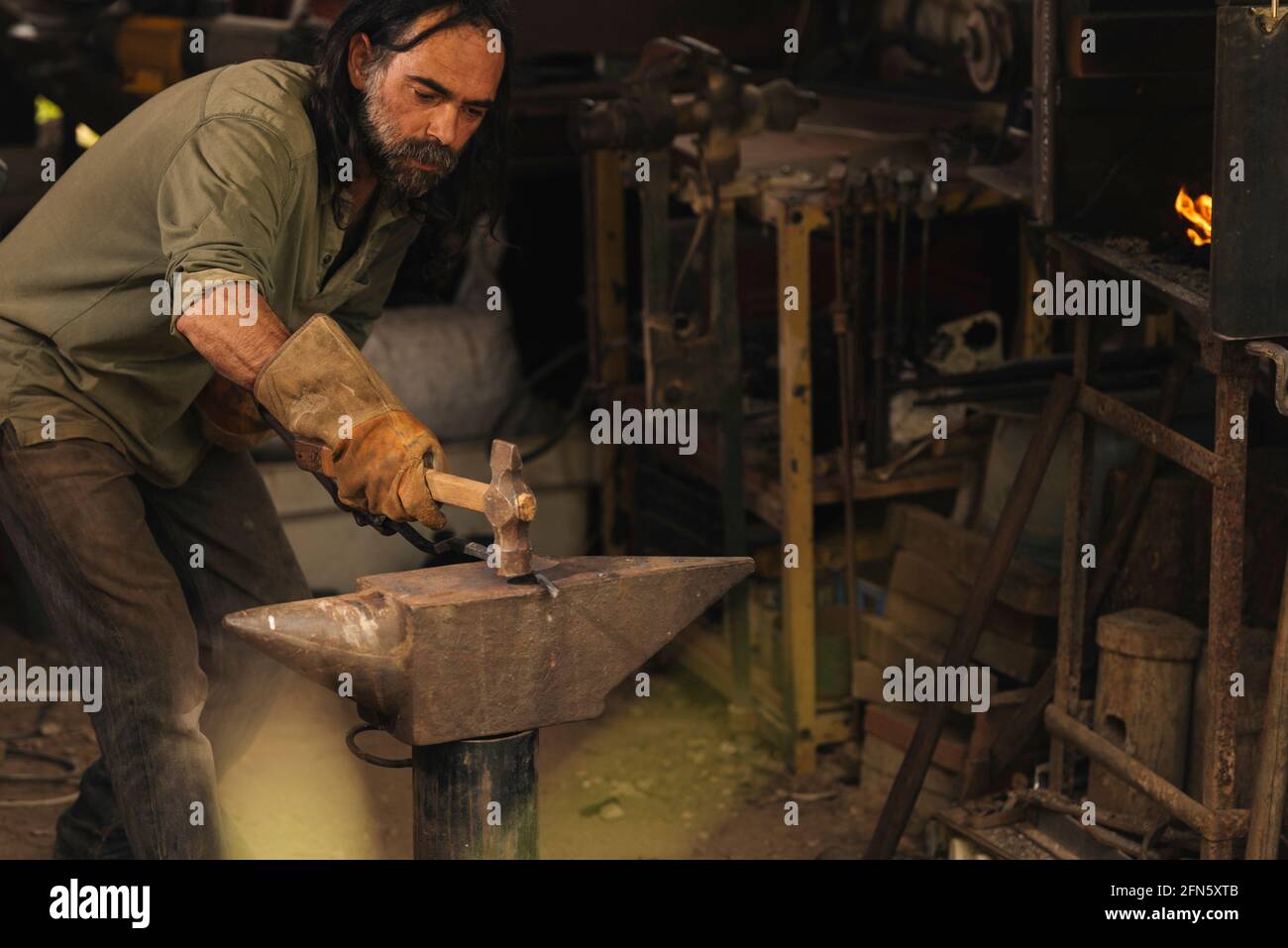 Blacksmith working a piece of steel with a sledgehammer on an anvil