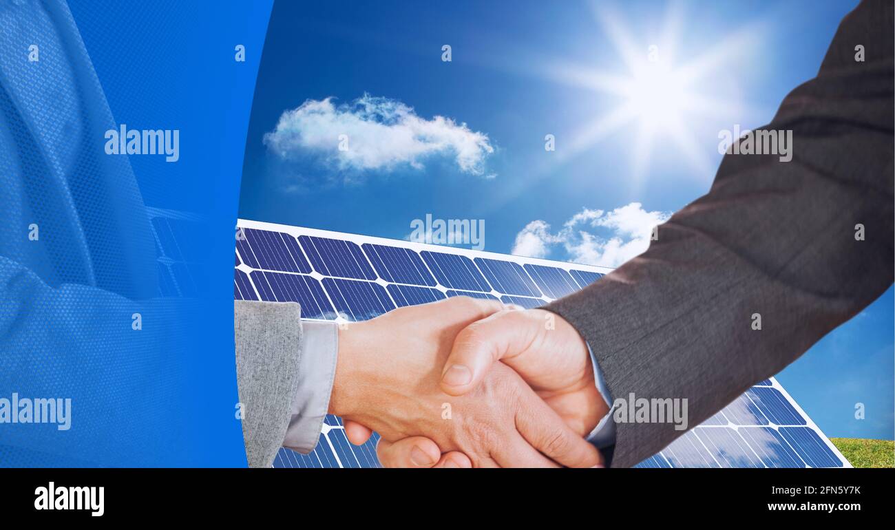 Mid section of two businessmen shaking hands over solar panel against blue technology background Stock Photo
