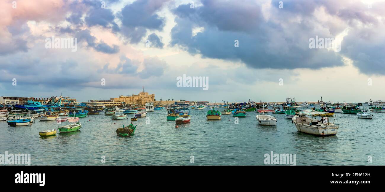 ALEXANDRIA, EGYPT - NOVEMBER 20, 2016: Cityscape with egyptian fisher boats, vessels and ships in the seaport at sunrise. Panoramic view with Qaitbay Stock Photo