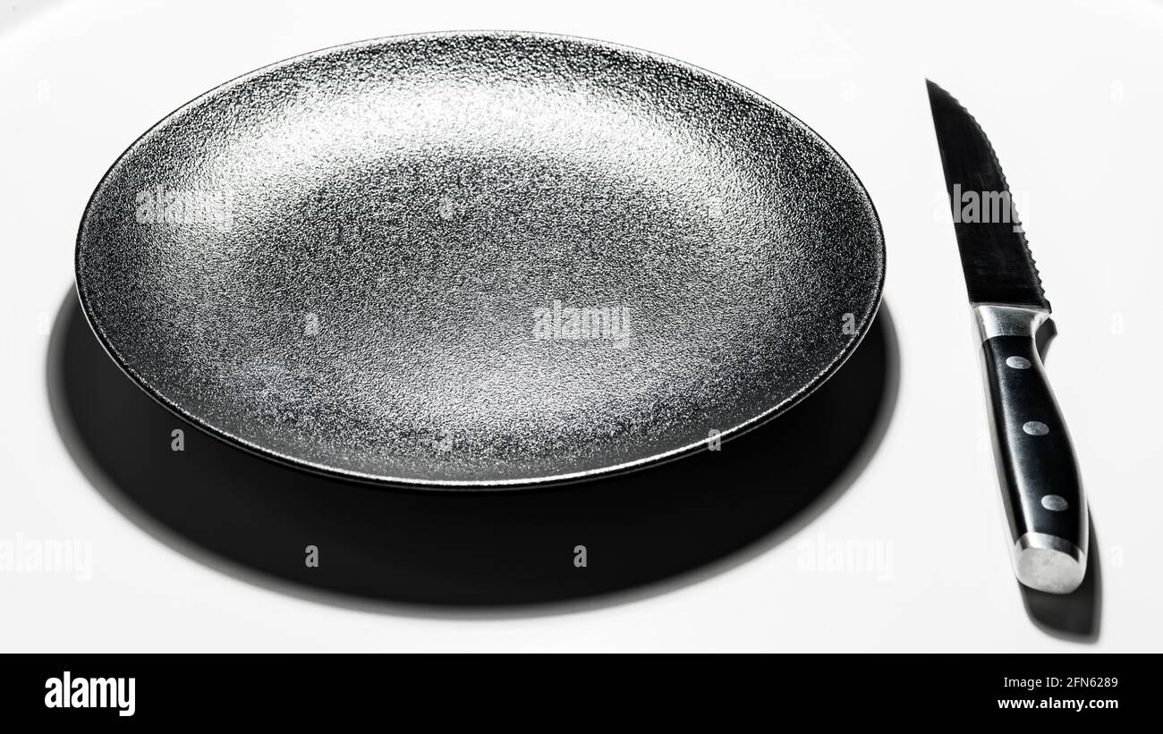 Black dessert plate and steel knife on white background Stock Photo