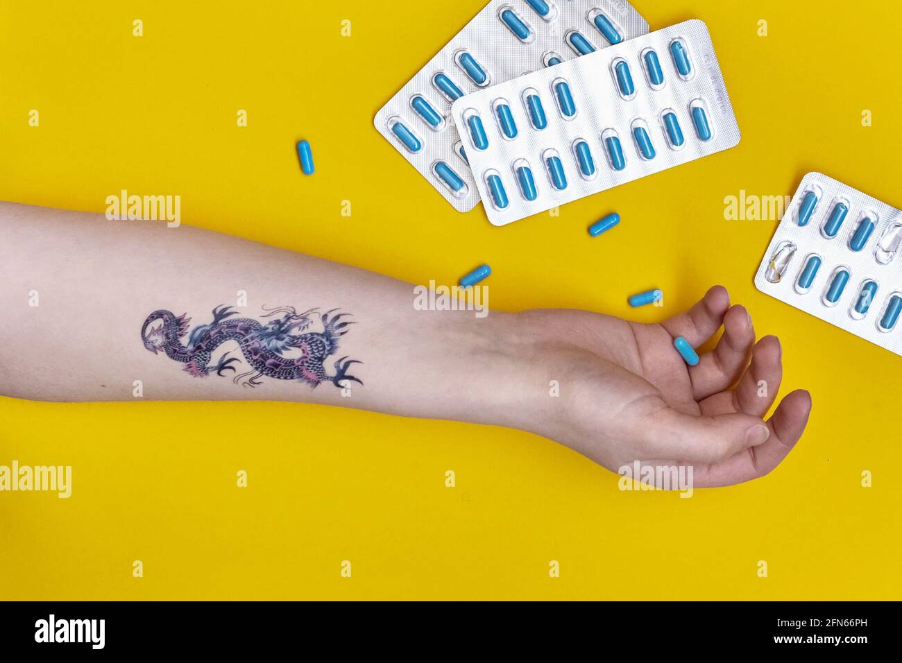 Female hand with a tattoo on a yellow background with scattered sleeping pills. Insomnia, depression, suicide concept. Stock Photo