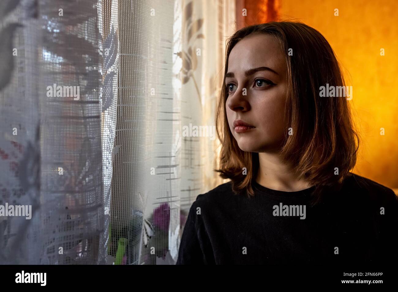 Portrait of a young teenage girl in a room by the window in the evening. Stock Photo