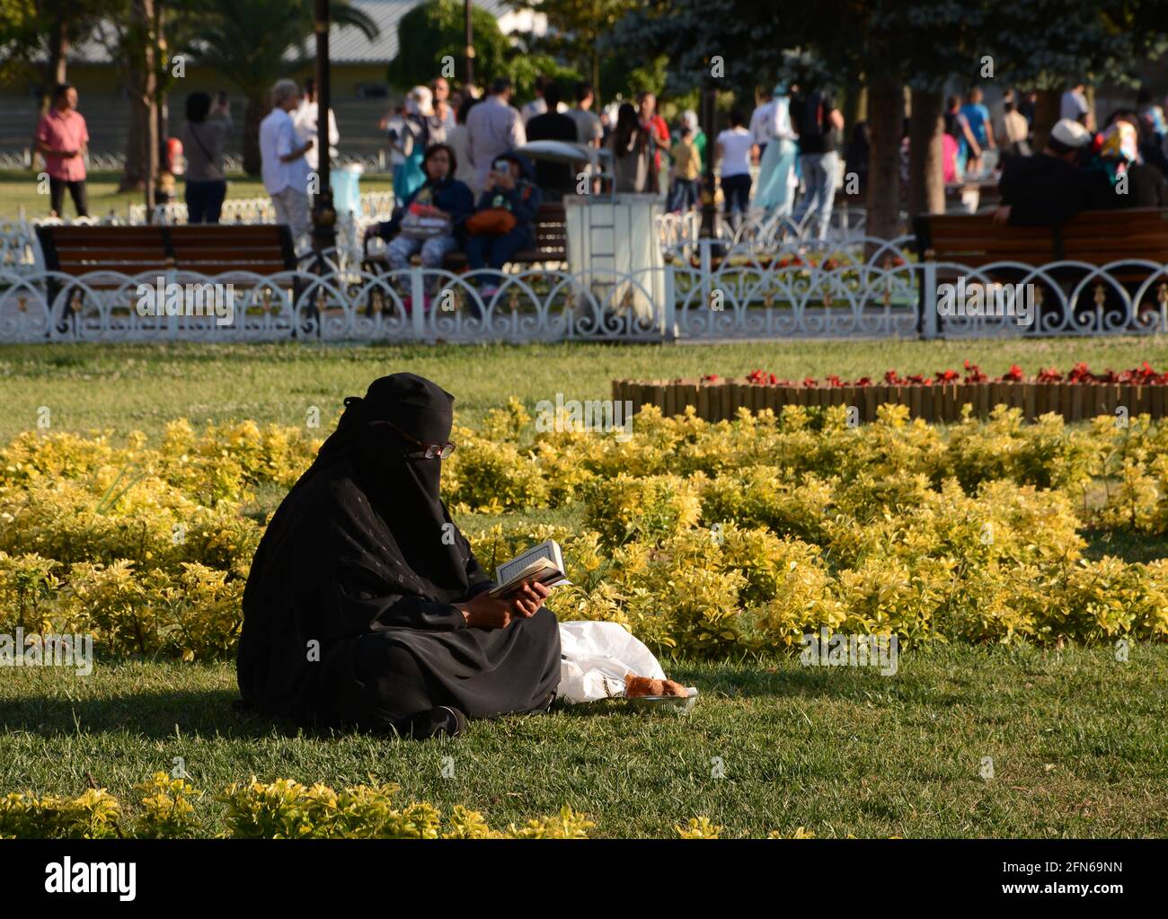 A lady wearing a burqa sat reading a book in Sultanahmet park in Istanbul. Traditional Islamic clothing worn by women to cover their whole body. Stock Photo