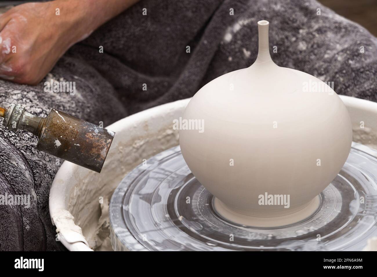 Potter / potters heat gun hotair / hot air to partially drive a clay whilst skilfully hand throwing a ceramic thrown clay vase pot on a turning wheel. England. UK (123) Stock Photo