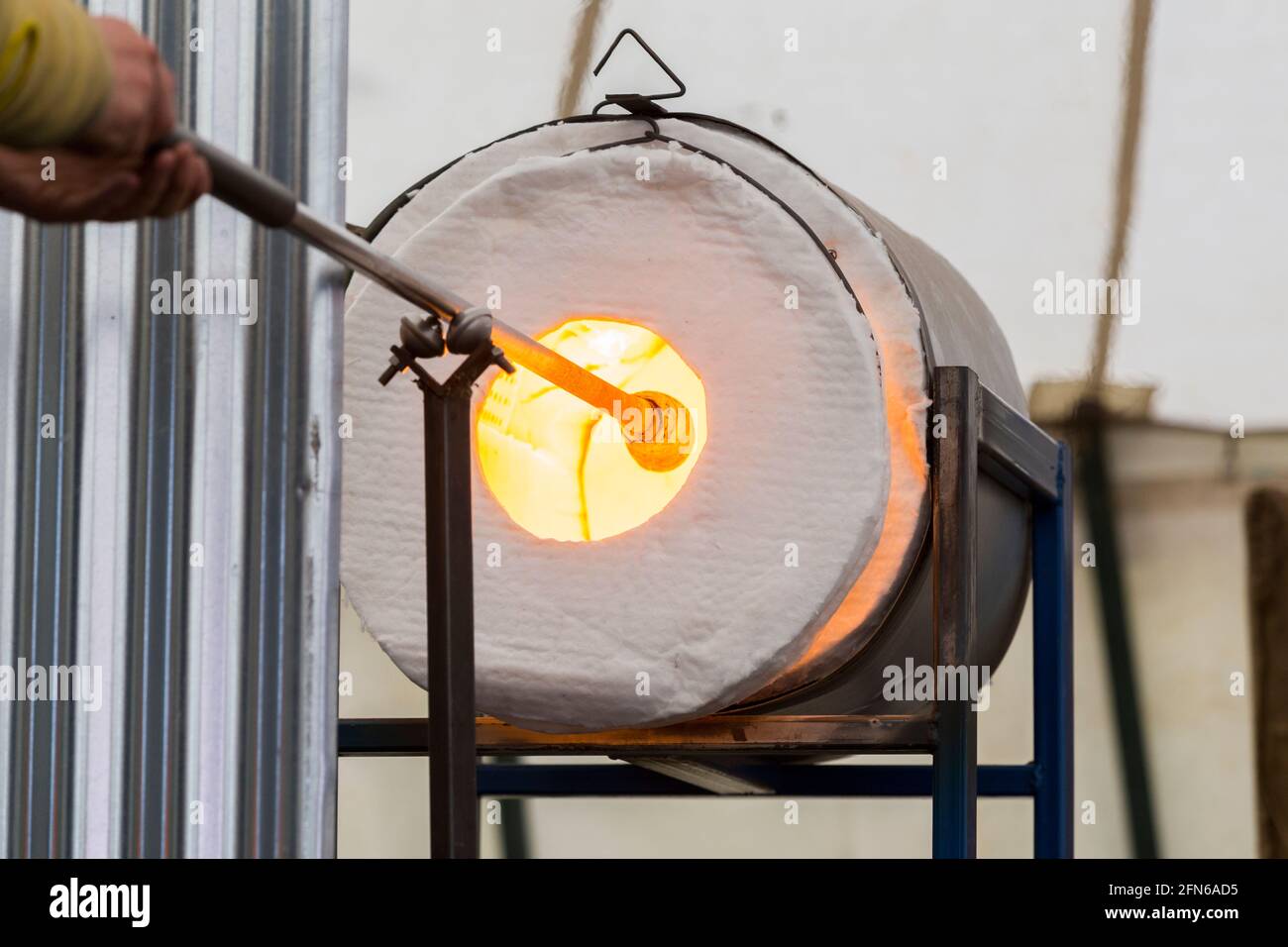 A glass blower uses a glory hole gas furnace to heat the glass gather on  the blowpipe  blow pipe  blow tube  blowtube and keep it molten before  his blowing