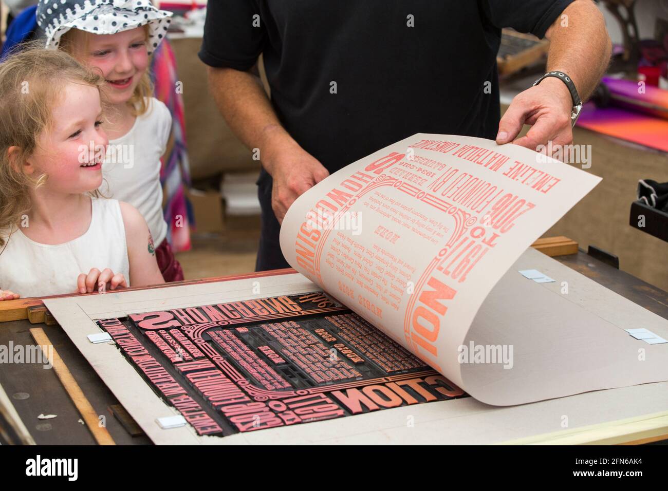 Sisters watch the hand made printing on a press of a poster print to celebrate Art in Action Festival Waterperry House, Oxfordshire, UK, in July, 2016. (123) Stock Photo