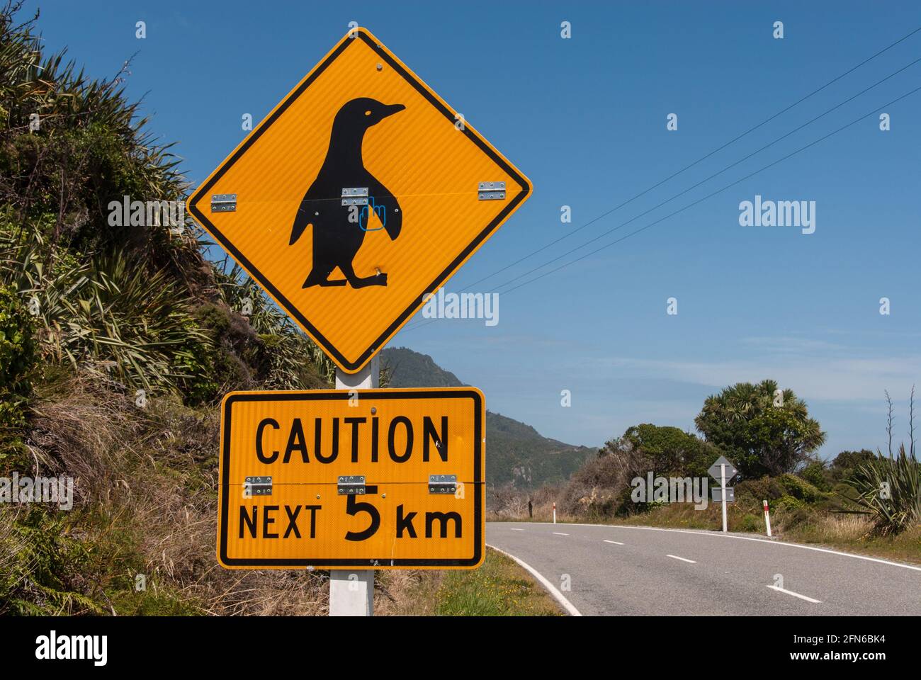 Achtung Pinguine kreuzen auf den nächsten 5 Kilometern! Warnschild an einer Küstenstraße im Westen der neuseeländischen Südinsel. - Caution penguins crossing next 5 km! Warning sign at a coastal road on the West coast of the South Island of New Zealand. Stock Photo