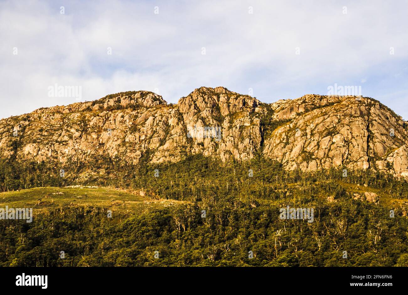 Rugged Tullah mountain landscape of Mount Farrell amongst green forest vegetation white clouds coverage in West Tasmania, Australia Stock Photo