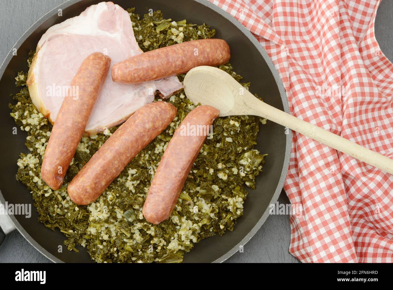 Fresh cooked kale with sausages, meat and wooden spoon  in the pan on black background Stock Photo