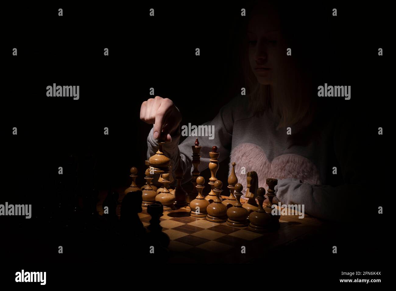 girl in the shadows plays vintage chess on a dark background. old chess. business concept Stock Photo