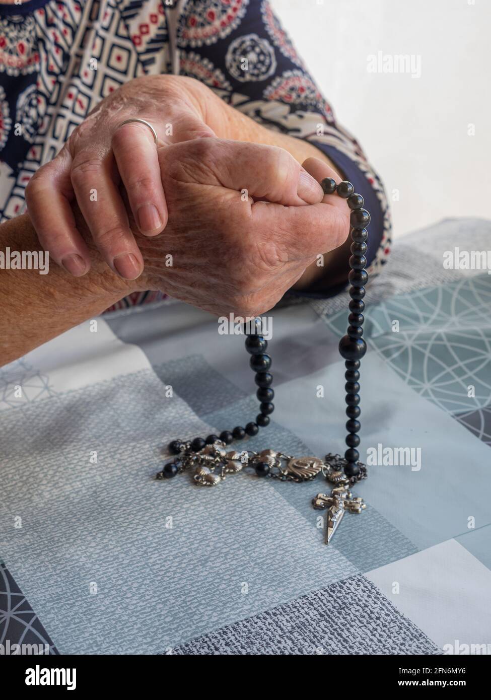 Hands of elderly woman praying with rosary and a crucifix in the linked ...