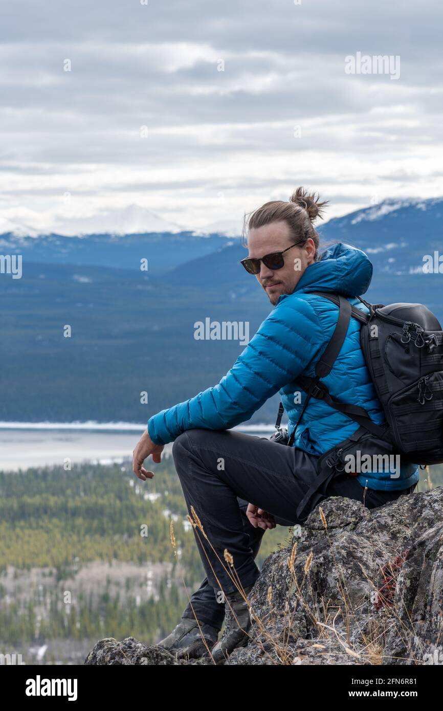 Man in blue jacket, black pants sitting on top of a mountain with