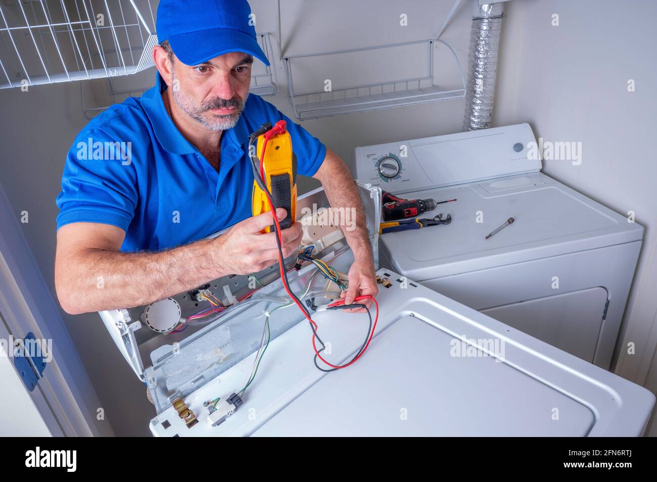 Appliance technician in uniform using a volt meter to troubleshoot a broken washing machine, looking at volt meter Stock Photo