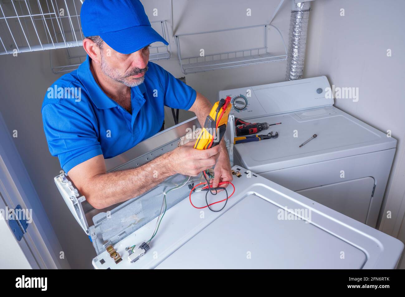 Appliance technician wearing a blue uniform testing circuits on a washing machine, looking at the volt meter Stock Photo