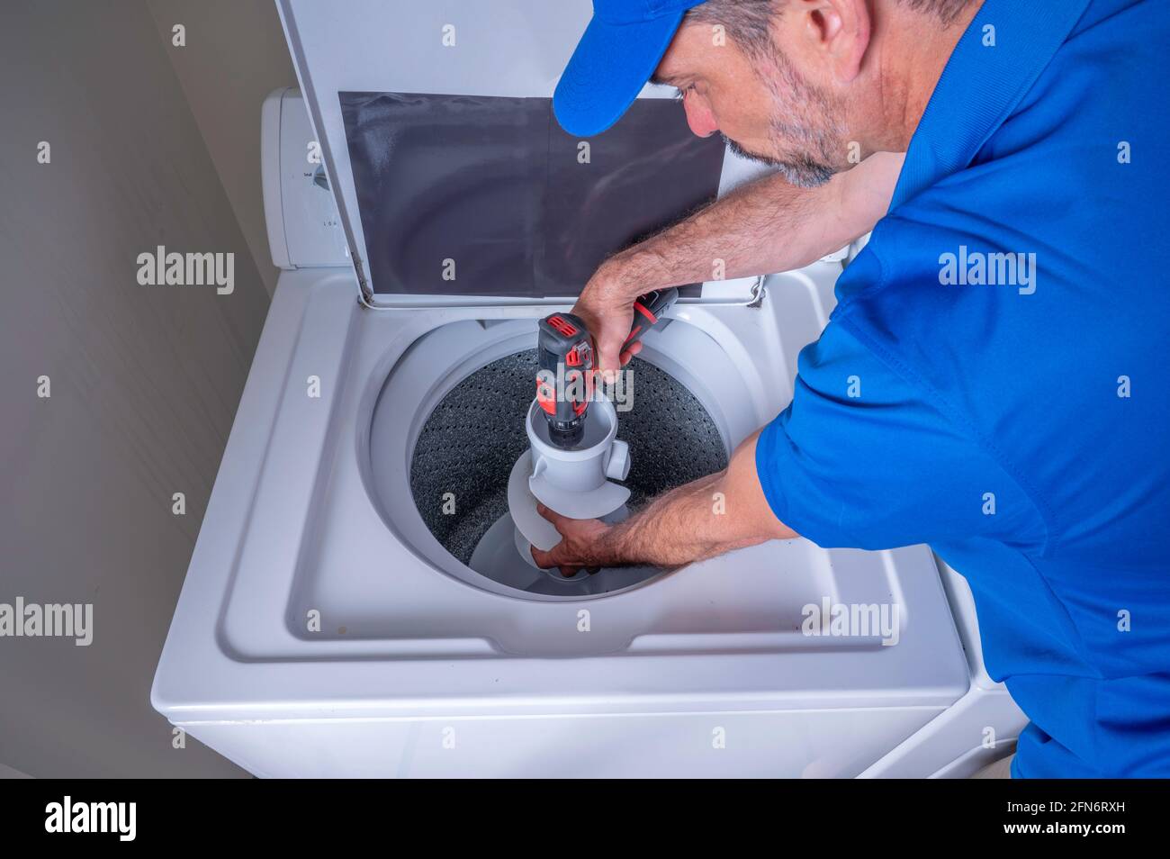 Appliance technician in a blue uniform installing a agitator on a washing machine, using a cordless drill Stock Photo