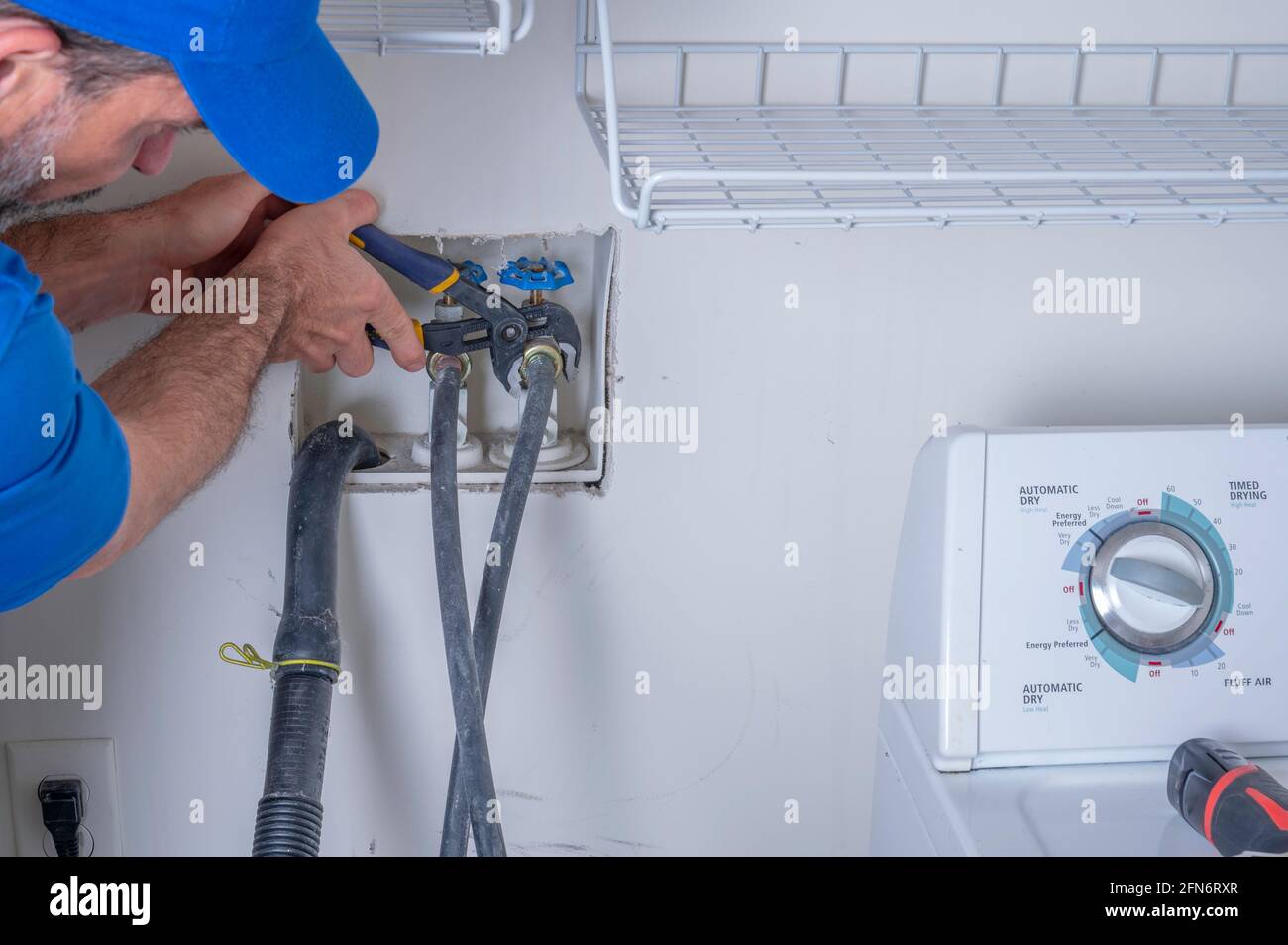 Plumber in a residential home hooking up water supply lines for a washing machine, appliance repair service Stock Photo