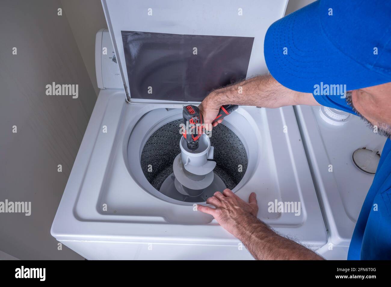 Appliance technician using a cordless drill to install a agitator for a residential washing machine in a home or an apartment Stock Photo