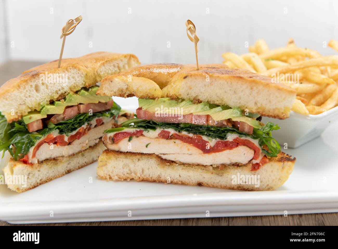 Layers loaded into this chicken sandwich stacked high with meat and fillings along with french fries. Stock Photo