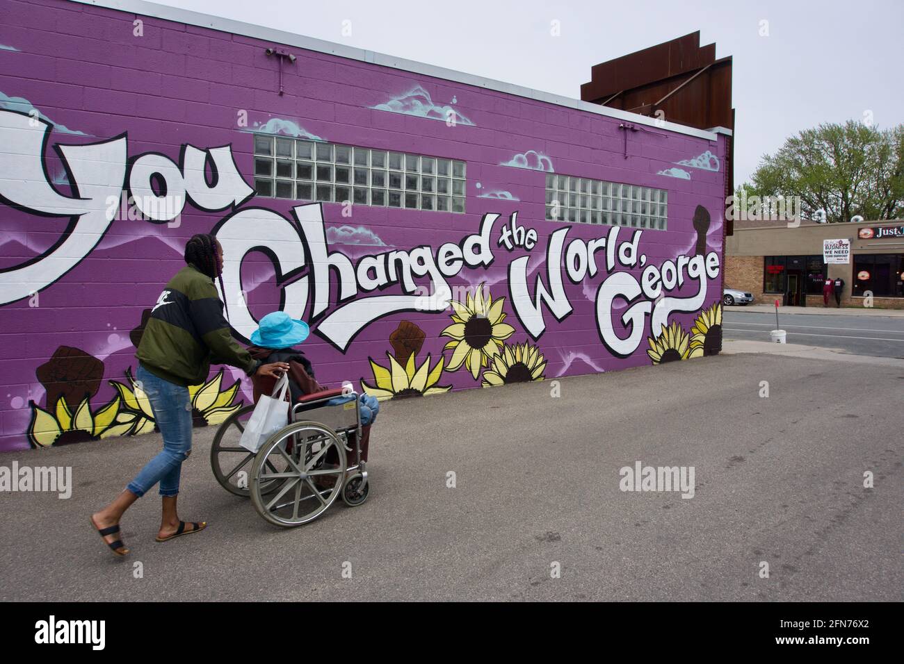 Woman pushing another in a wheelchair at George Floyd Square in front of a mural that says 'You Changed The World, George'. Minneapolis, MN, USA Stock Photo