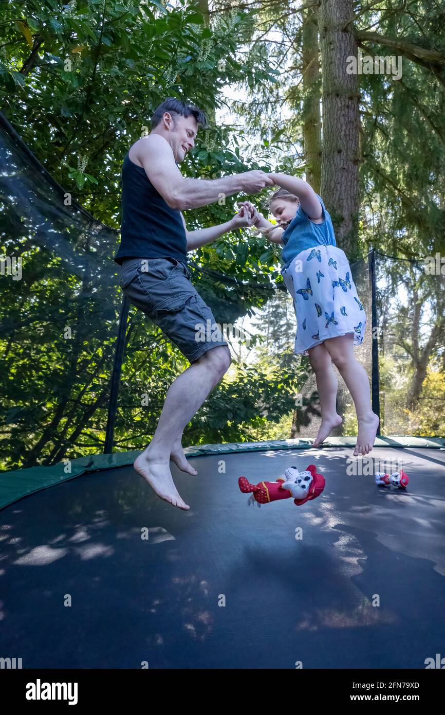 Lynwood, Washington, USA.  Four year old girl and her father bouncing on a trampoline in their backyard. Stock Photo