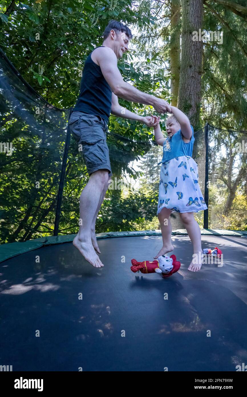 Lynwood, Washington, USA.  Four year old girl and her father bouncing on a trampoline in their backyard. Stock Photo
