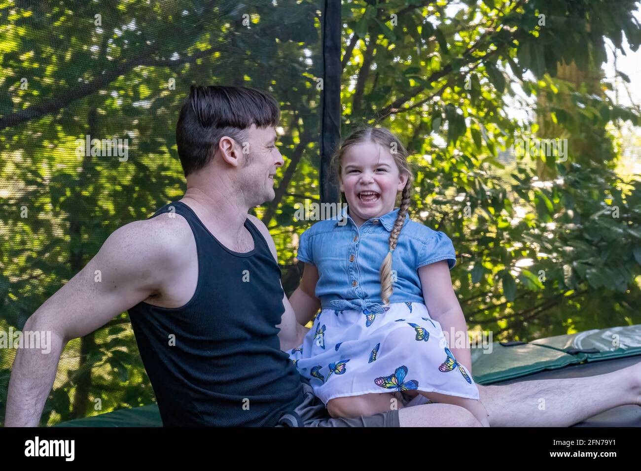 Lynwood, Washington, USA.  Father and four year old daughter taking a rest on their backyard trampoline after playtime. Stock Photo