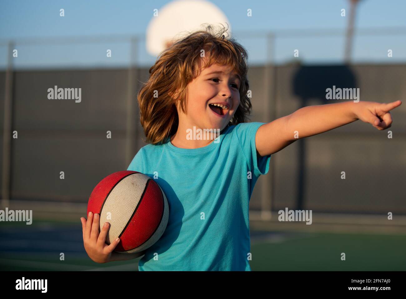 Happy smilin kid playing basketball, pointing showing gesture. Activity and sport for kids. Stock Photo