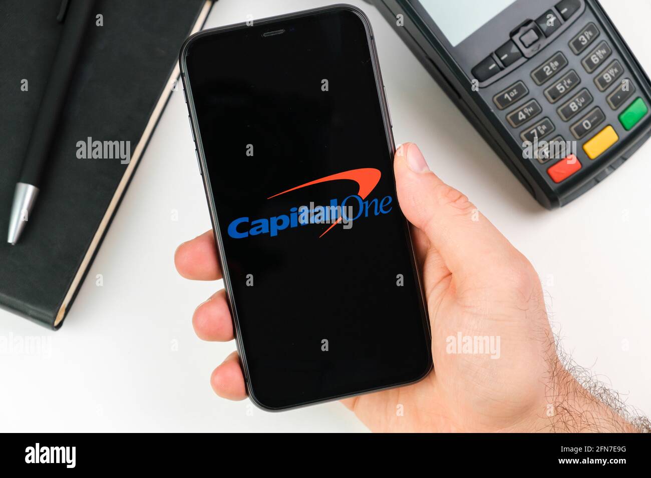 Capital One bank logo on the black smartphone screen in mans hand on the background of payment terminal, May 2021, San Francisco, USA Stock Photo