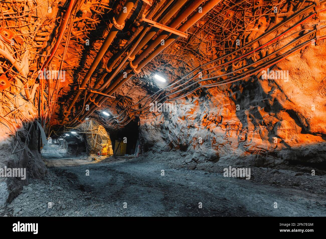 Tunnel of the mining of an underground mine. Lots of pipelines on the ceiling and rail track for trolleys Stock Photo