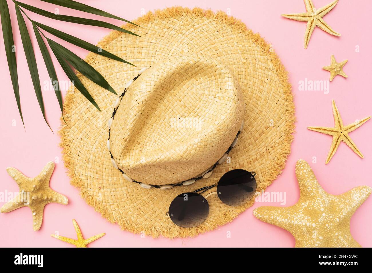 Womens straw hat, sunglasses, starfish and palm leaf on a pink ...
