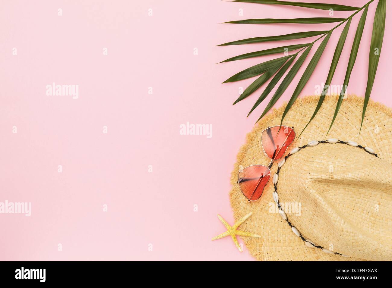 Ladies straw hat, sunglasses and palm leaf on pink background with copy ...