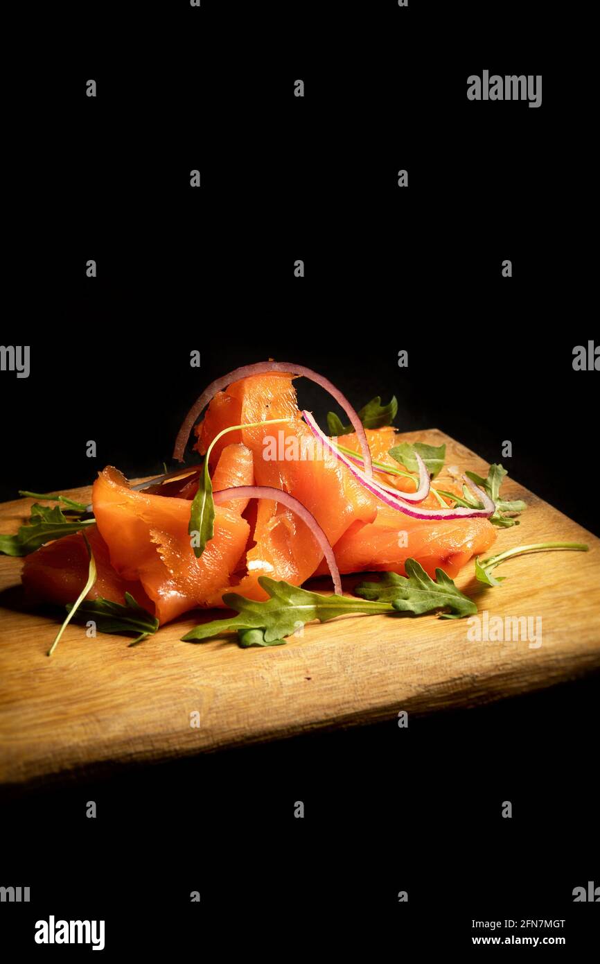Smoked salmon sliced and arranged with arugola a popular appetizer, on a wooden plate end a black background Stock Photo
