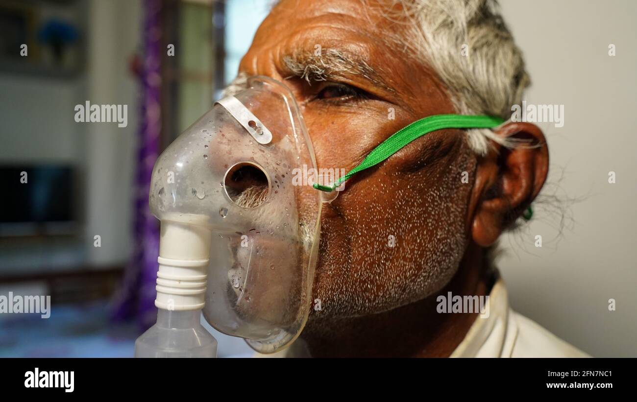 03 May 2021- Reengus, Sikar, India. Old Indian man infected with Covid 19 disease. Patient inhaling oxygen wearing mask with liquid Oxygen flow. Stock Photo