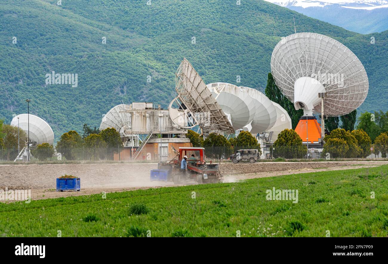 Contrasts of technologies in the Fucino plain. Satellite communication antennas and farm workers who collect carrots. Fucino, Abruzzo, Italy, Europe Stock Photo