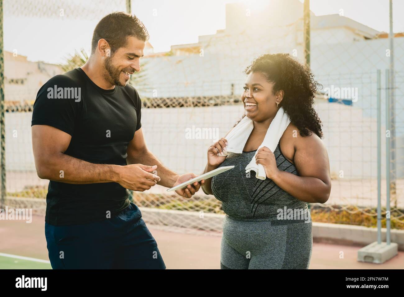 Personal trainer working with curvy woman while giving her istruction with digital tablet during training session - Sport people lifestyle concept Stock Photo