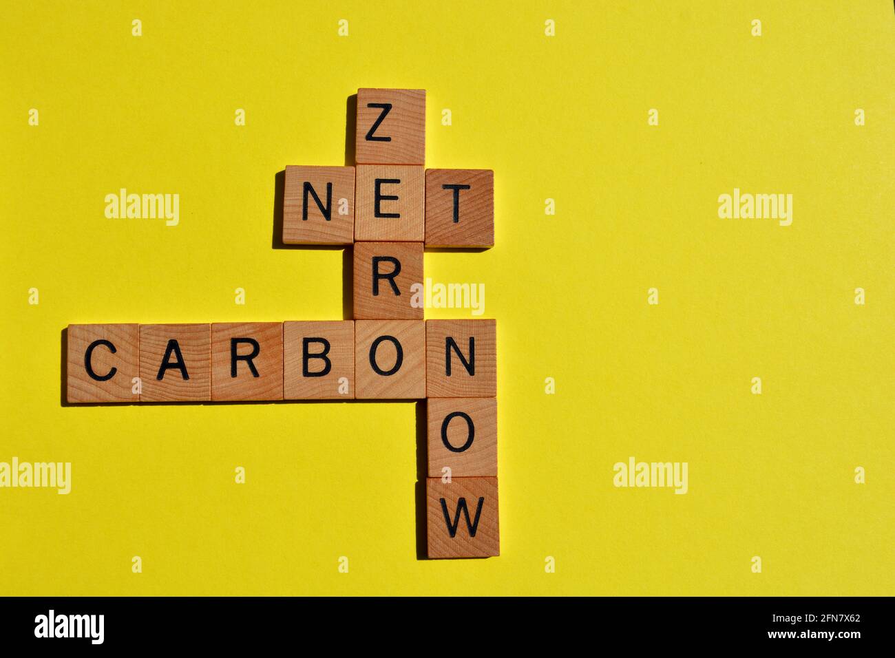 Net, Zero, Carbon, Now, words in wooden alphabet letters in crossword form isolated on yellow background with copy space Stock Photo