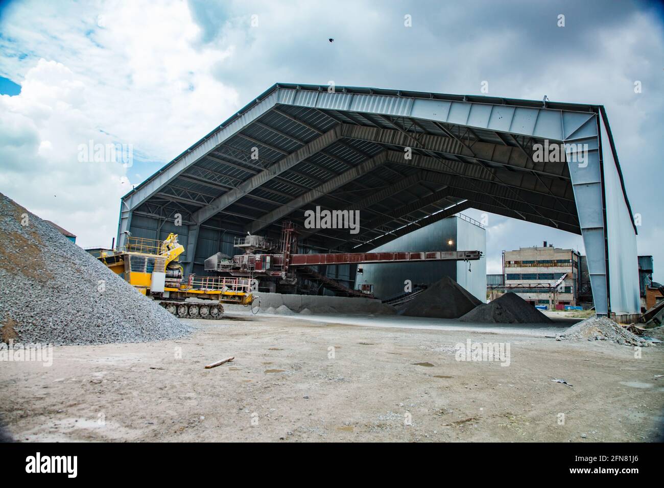 Temirtau, Kazakhstan - June 09, 2012: Old outdated Soviet cement plant. Storage of raw materials. Loading machine under the roof and heaps of stones. Stock Photo