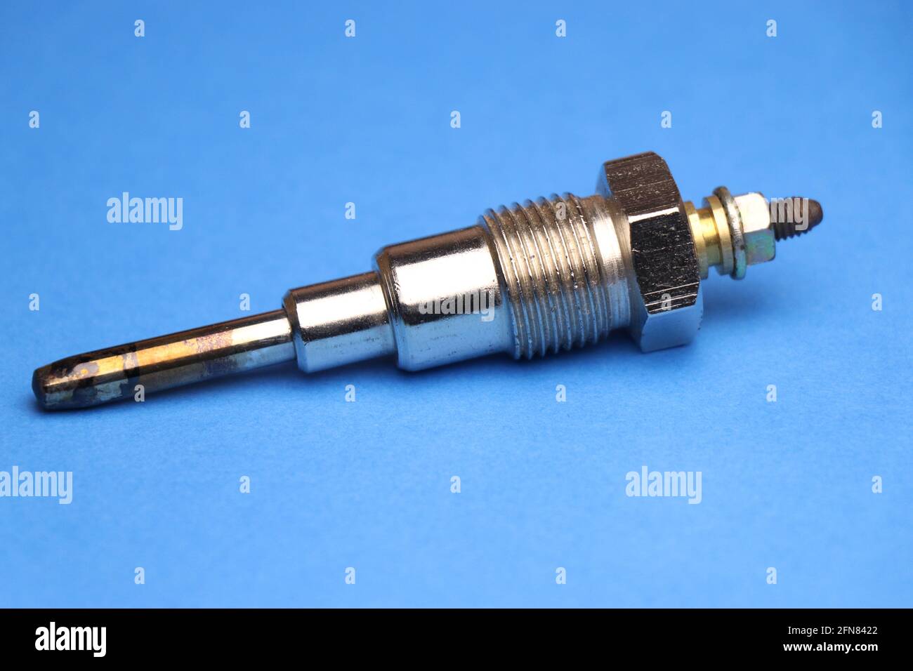 Glow plug for diesel engine which is auto spare part that is necessary for engine to start by heating the internal combustion part on blue background Stock Photo