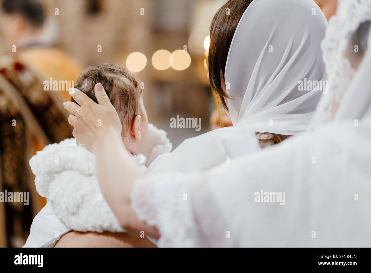 The sacrament of baptism. Mom strokes the child on the head in church. Stock Photo