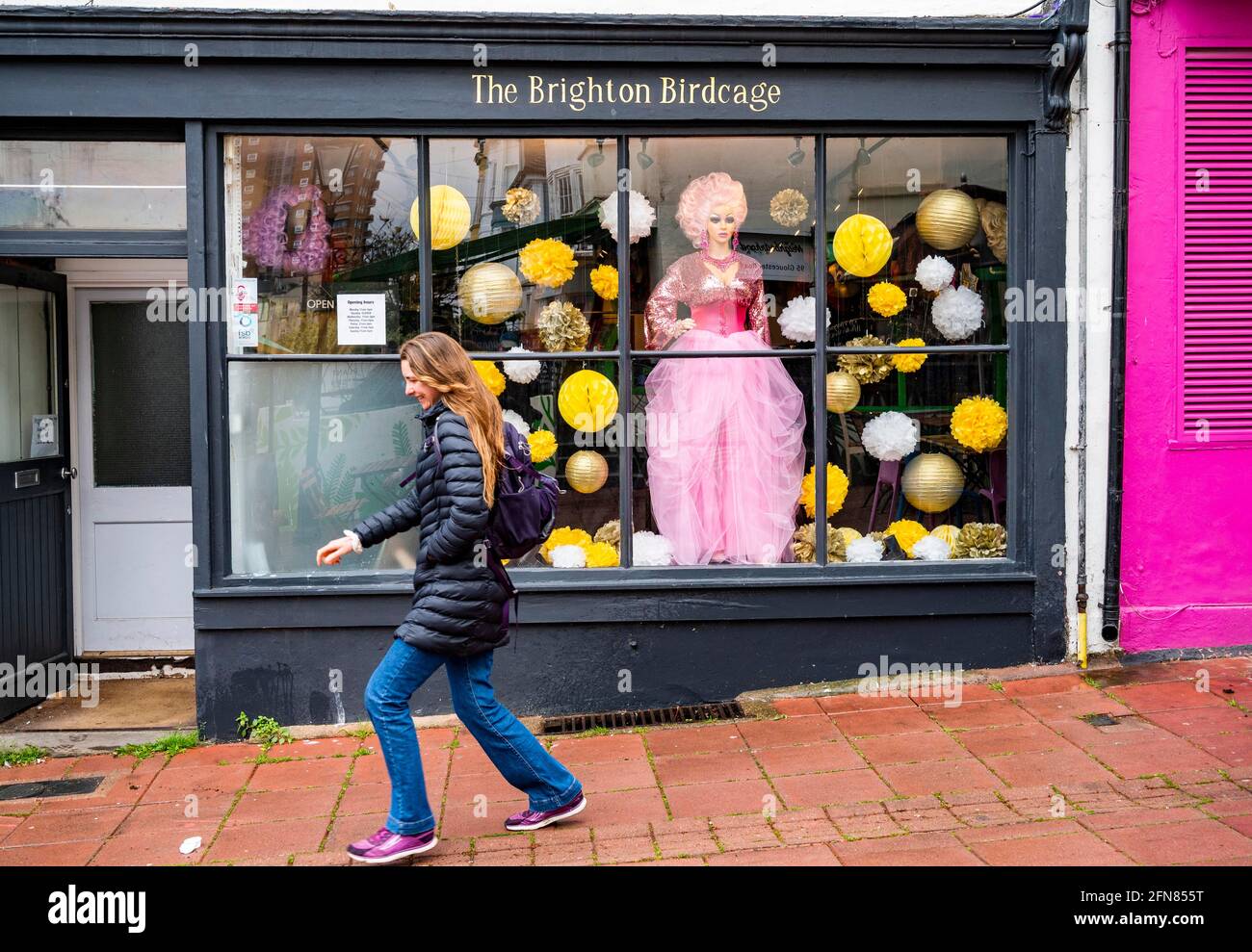 Brighton UK 15th May 2021 - A young lady dashes down the street past the Brighton Birdcage shop in Brighton as wet weather sweeps across most parts of Britain today : Credit Simon Dack / Alamy Live News Stock Photo