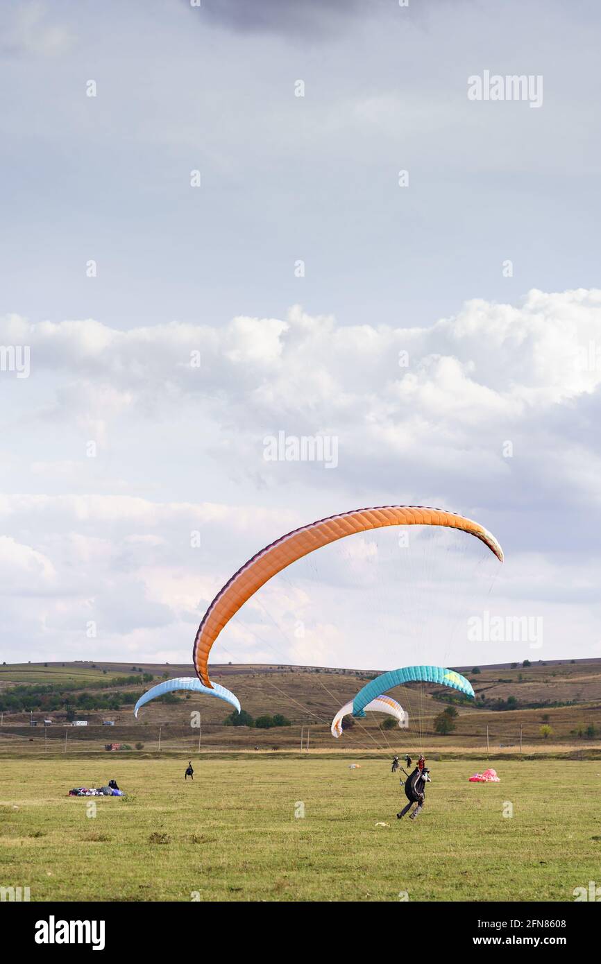 Paragliders silhouette flying over beautiful green landscape under blue sky with clouds. Paragliding school, practice Stock Photo