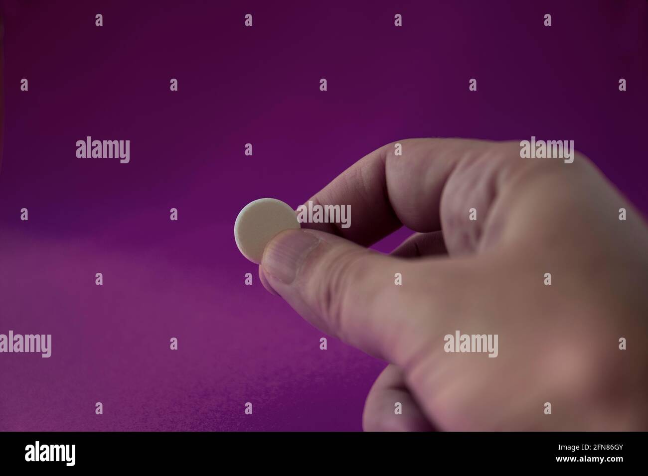 Hand and fingers holding medicine capsule in front of purple background. selective focus  pill. Stock Photo