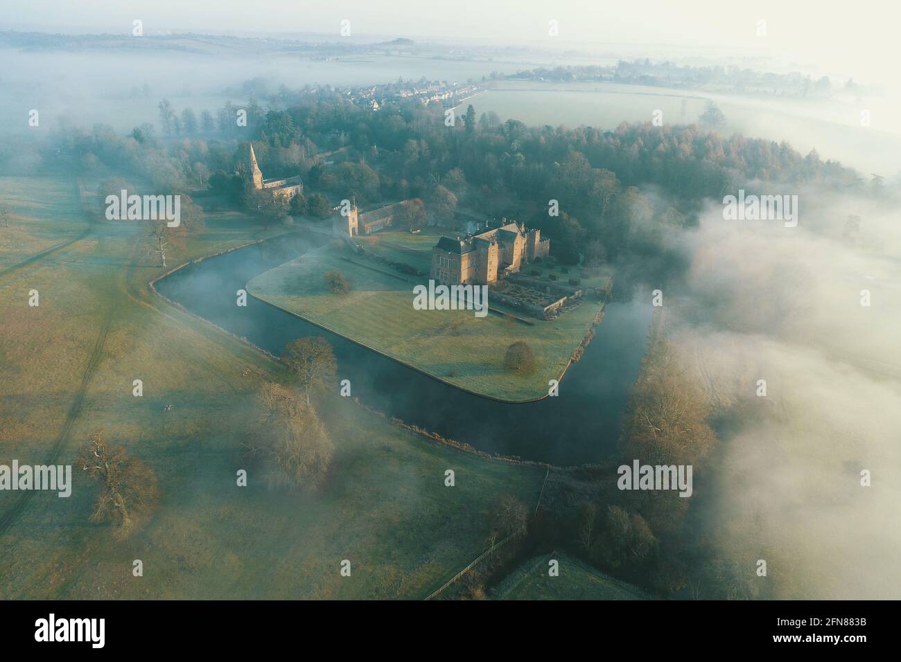 DCIM117MEDIADJI 0144.JPG Dramatic aerial drone image of Broughton Castle, moat and Park lit by sunshine at dawn and emerging from a bank of fog Stock Photo