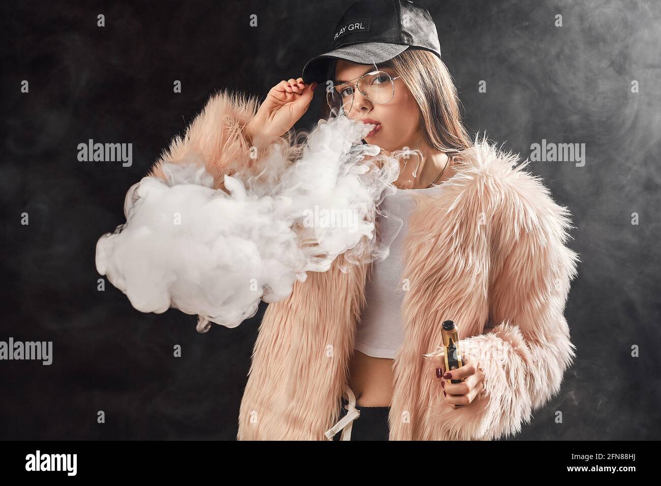 Sexy trendy rap woman in pink fur coat and cap smoke electronic 